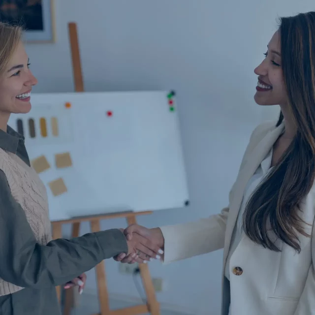 Deux femmes se serrent la mains en souriant devant un tableau montrant des statistiques